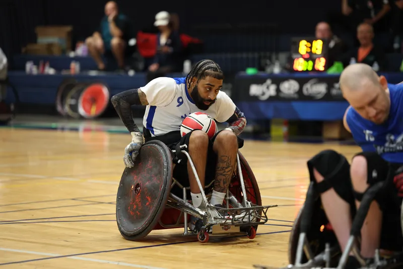 A smiling player raises the ball overhead while an opponent stretches to block